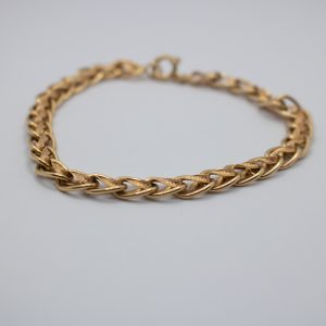 Vista aproximada de pulseira em ouro com desenho em espiral entrançada.